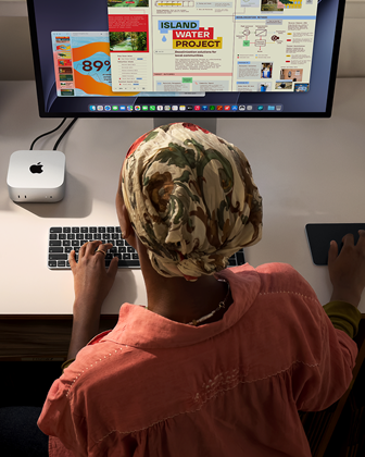 Iemand die typt aan een bureau met een Mac mini, Studio Display aangesloten, Magic Keyboard, Magic Trackpad, diverse items