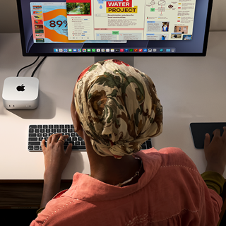 Iemand die typt aan een bureau met een Mac mini, Studio Display aangesloten, Magic Keyboard, Magic Trackpad, diverse items